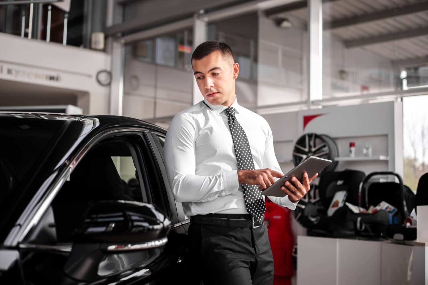Asesor de servicio con tableta junto al auto del cliente